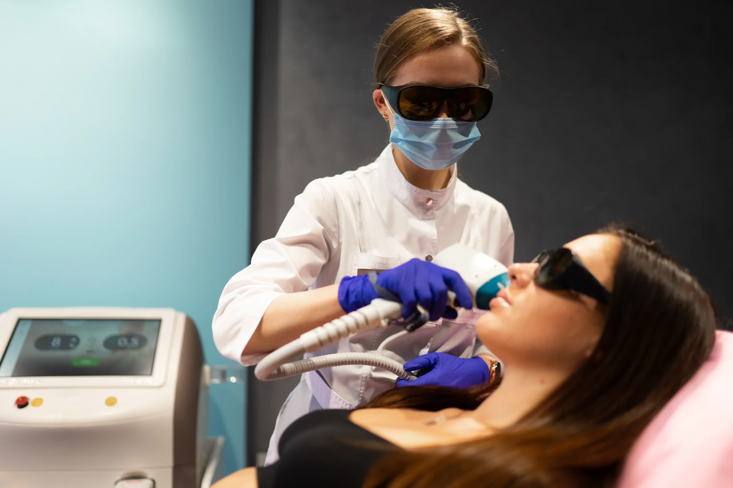 Medical aesthetician performing facial laser hair removal on a female patient wearing protective eyewear.